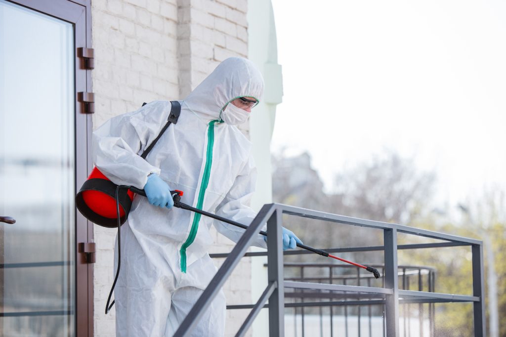 Coronavirus Pandemic. A disinfector in a protective suit and mask sprays disinfectants in the room. Coronavirus Pandemic. A disinfector in a protective suit and mask sprays disinfectants in the room. Protection of COVID-19 disease. Prevention of spreding pneumonia virus with surfaces we touch.